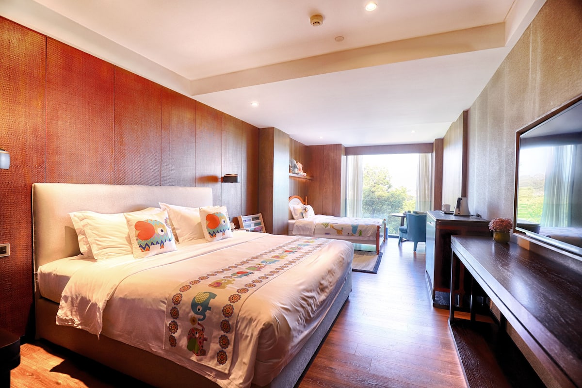 A modern hotel room with a large bed, a desk, and a view of the outdoors.