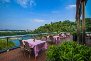 Un espace extérieur aménagé pour les repas, avec des tables et des chaises, offrant une vue sur une rivière et la verdure environnante.