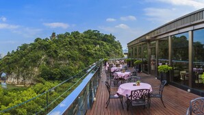 Un restaurante a orillas del río con terraza al aire libre que ofrece vistas de un río y una colina boscosa.