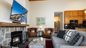 A living room with a fireplace, a television, leather armchairs, a sofa, and a kitchen in the background. - Villas at Snowmass Club - 1533 ~ Snowmass Club Access ~ (Snowmass Village)