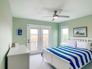 Ein Schlafzimmer mit einem Bett, einem Deckenventilator, einem Schreibtisch und einer Tür, die auf einen Balkon führt.