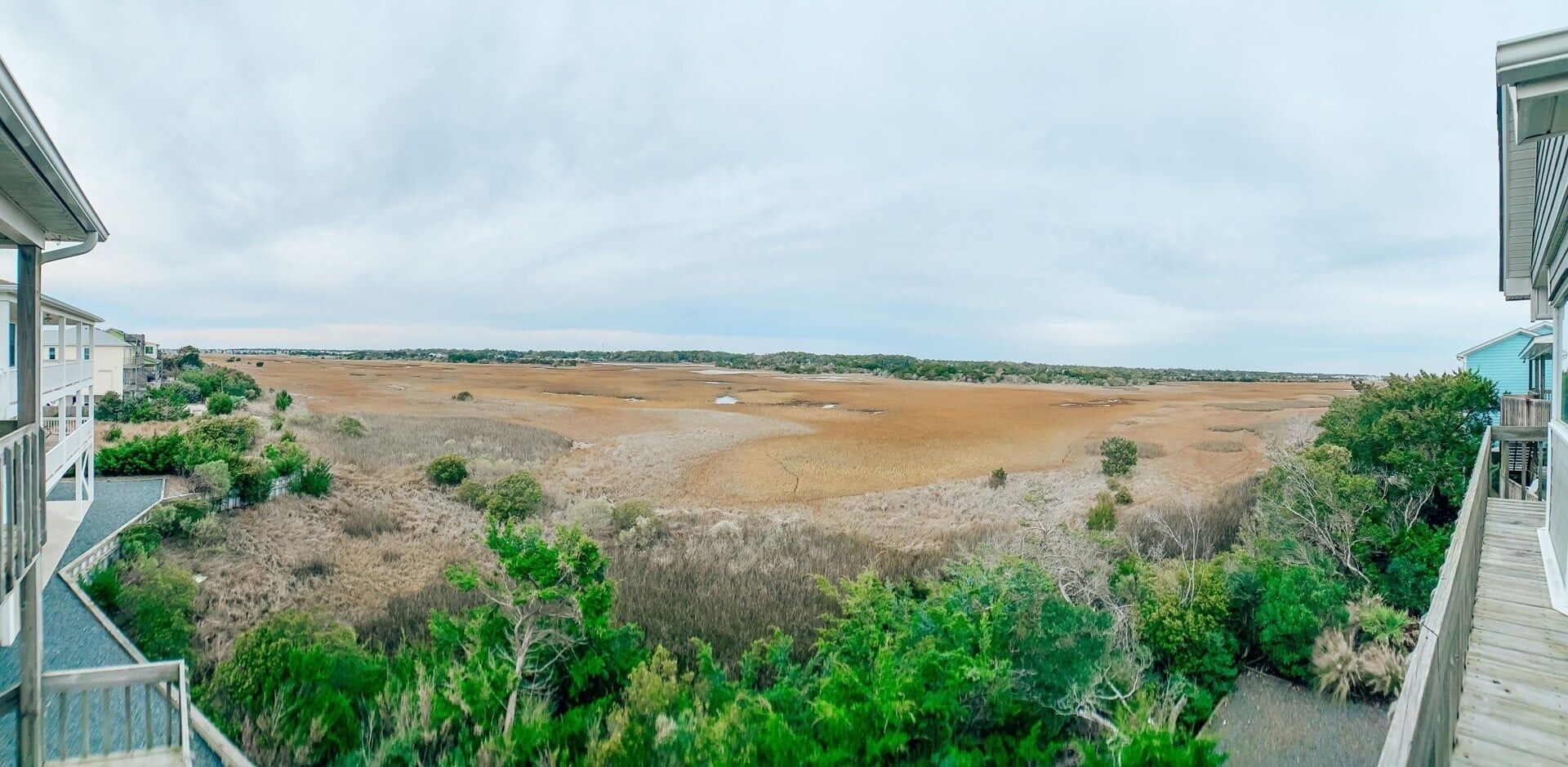 A view of a coastal landscape with a building on the left and a wooden deck on the right.