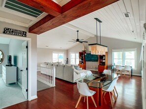 A spacious living area with a glass dining table, white sofas, and a kitchen with a TV. - A Beach To Remember 4 Bedroom Home by RedAwning (Supply)