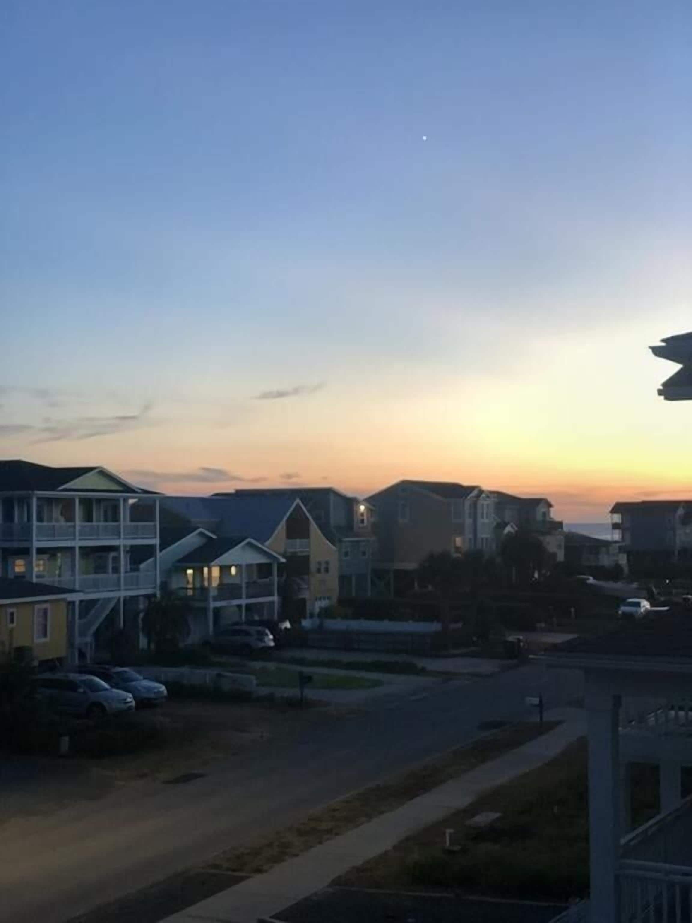 Un quartier résidentiel avec des maisons et des voitures garées, au coucher du soleil.