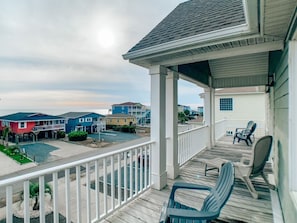 A coastal residential area with a wooden deck and chairs, a covered porch, and houses in the background. - A Beach To Remember 4 Bedroom Home by RedAwning (Supply)