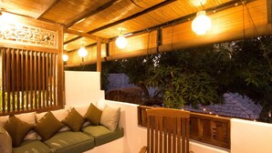 A cozy outdoor seating area with a wooden bench and a cushioned sofa, a wooden table, and a view of greenery through a window. - The Mandana Gili Air (Gili Air)