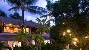 A thatched-roof building with large windows and a balcony, surrounded by lush greenery and palm trees. - The Mandana Gili Air (Gili Air)