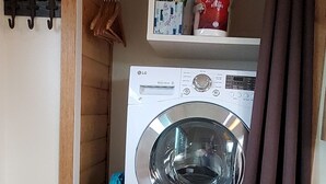 A laundry room with a front-loading washing machine, a dryer, and a shelf with cleaning supplies. - The Taiga 2, Studio Apartment (Healy)