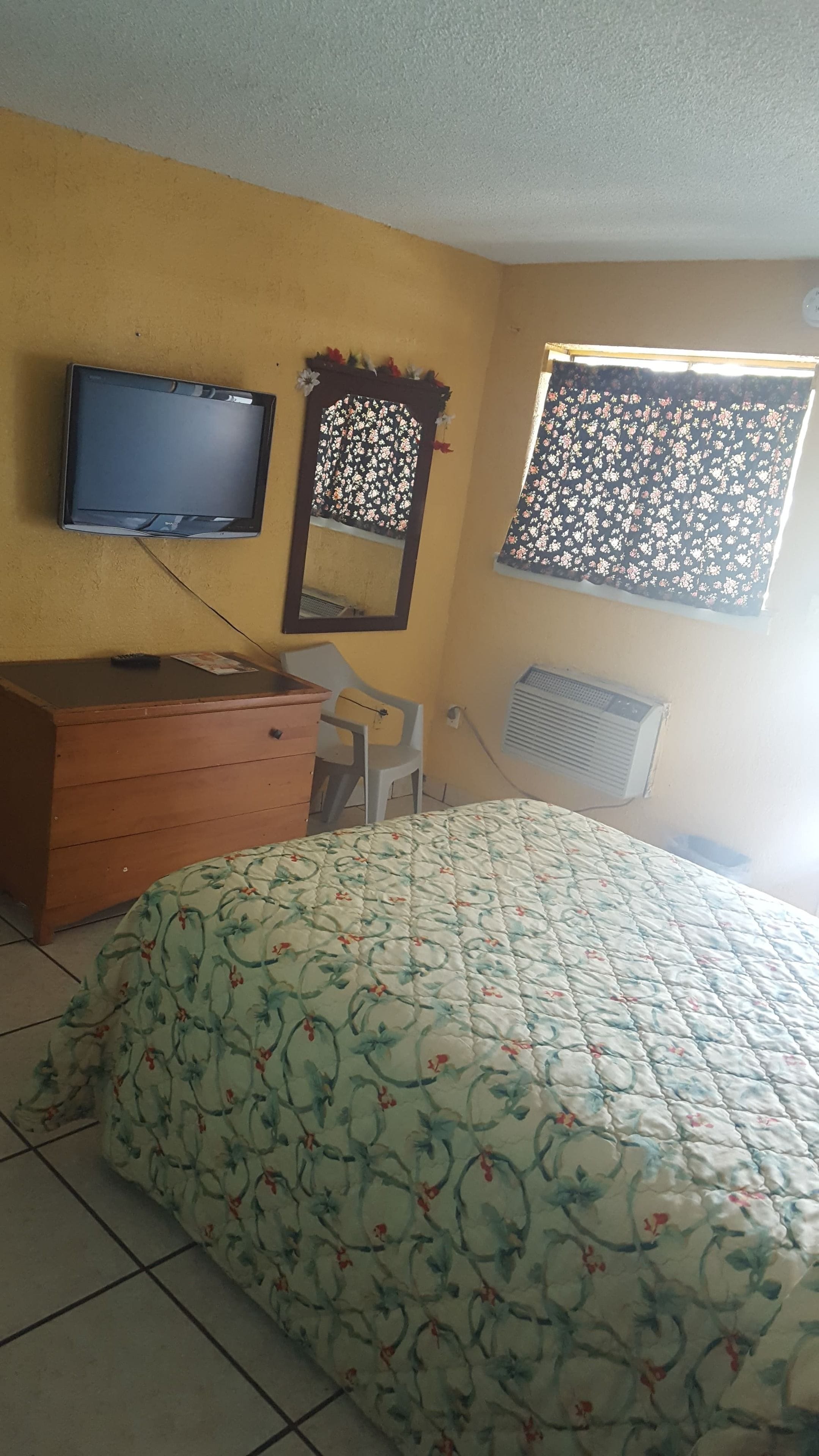A room with a bed, a dresser, a television, a window with a curtain, and an air conditioning unit.