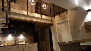 A modern kitchen with a brick backsplash, pendant lighting, and a dining area with a wicker chair.