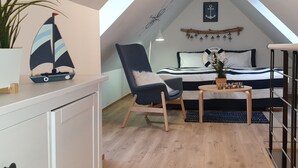 A cozy attic bedroom with a sloped ceiling, a sailboat decoration, a chair, a bed with a 'WELCOME' sign, and a small table with a plant.