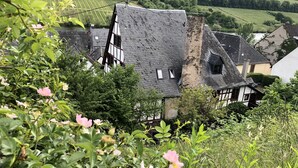 Une maison traditionnelle à colombages, dotée d’un toit à forte pente, entourée d’une végétation luxuriante et avec une rivière en arrière-plan.