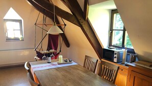Un coin repas avec une table en bois, des chaises, un luminaire suspendu, une bouteille de vin et une bougie.