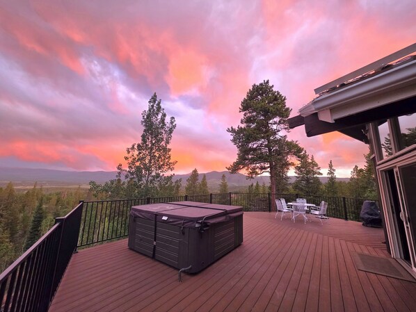 A deck with a hot tub, outdoor seating, and a view of mountains.