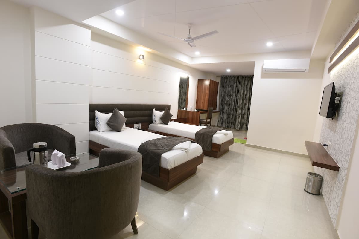A modern hotel room with two single beds, a small table with a coffee maker, and a seating area with chairs.