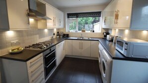 A modern kitchen with white cabinets, a gas stove, a microwave, and a built-in washing machine. - Charming Village house in Bramhall near Manchester (Bramhall)