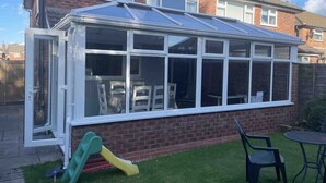 A conservatory with a glass roof, a brick wall, and a small garden area with a slide and chairs. - Charming Village house in Bramhall near Manchester (Bramhall)