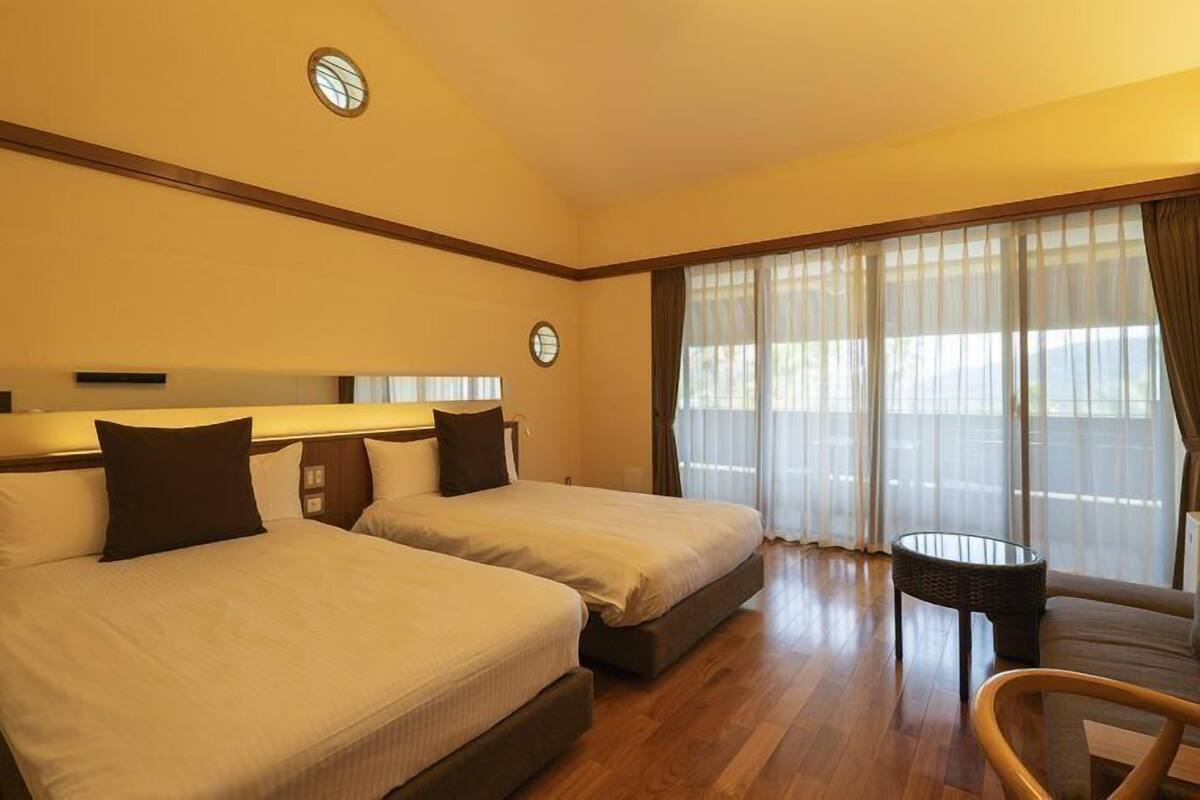 Quarto de hotel com duas camas, uma mesinha e um sofá.