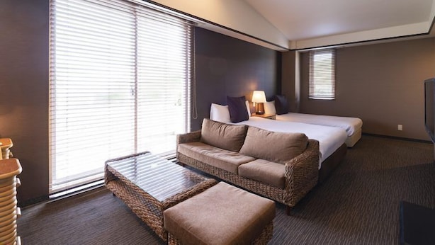 A hotel room with a bed, a sofa, a small table, and a TV. - Shonan OVA (Yokosuka)
