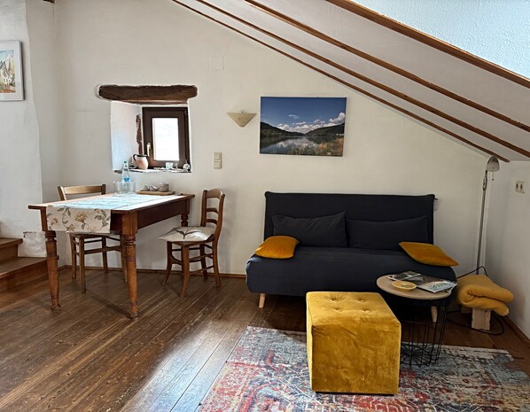 Un salon chaleureux avec un canapé bleu foncé, une table à manger en bois et un pouf jaune.