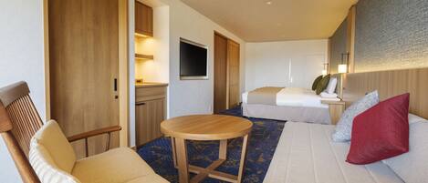A hotel room with a sofa, a chair, a small table, a bed, a TV, and a bathroom with a shower and toilet.