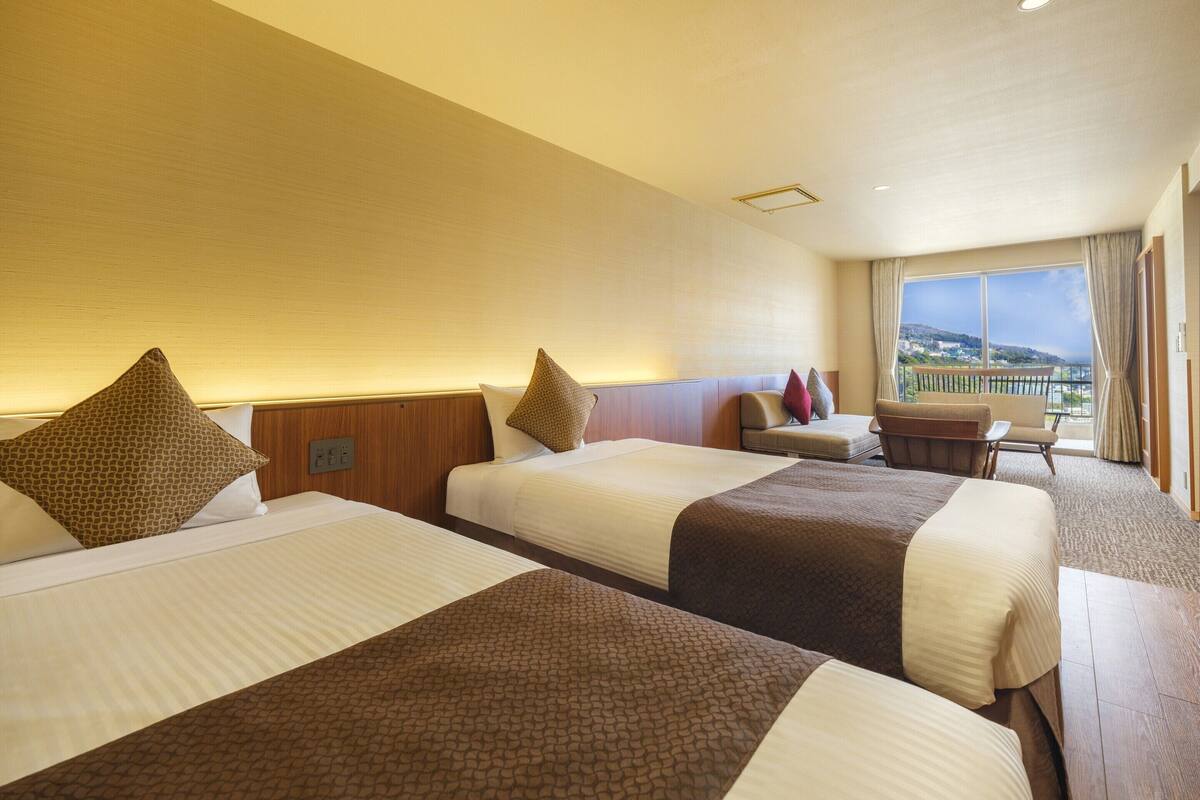 Een hotelkamer met drie bedden, een zithoekje en een balkon met uitzicht.
