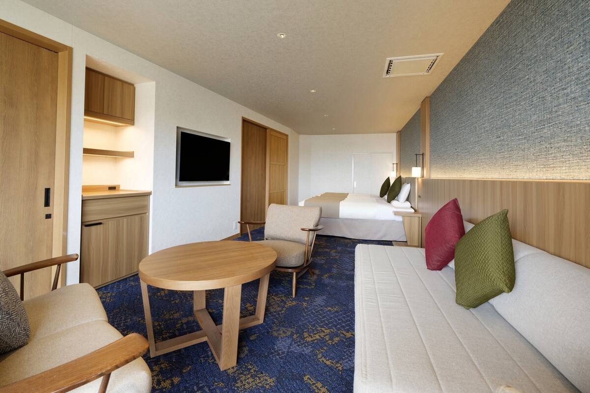 Een hotelkamer met een bed, een bank, een klein tafeltje, een stoel, een televisie en een kledingkast.