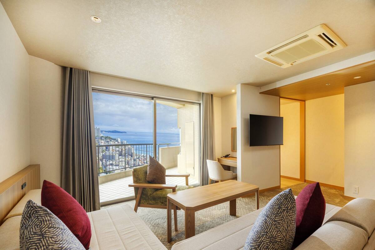 Een hotelkamer met balkon, een bank, een tafel en een televisie.