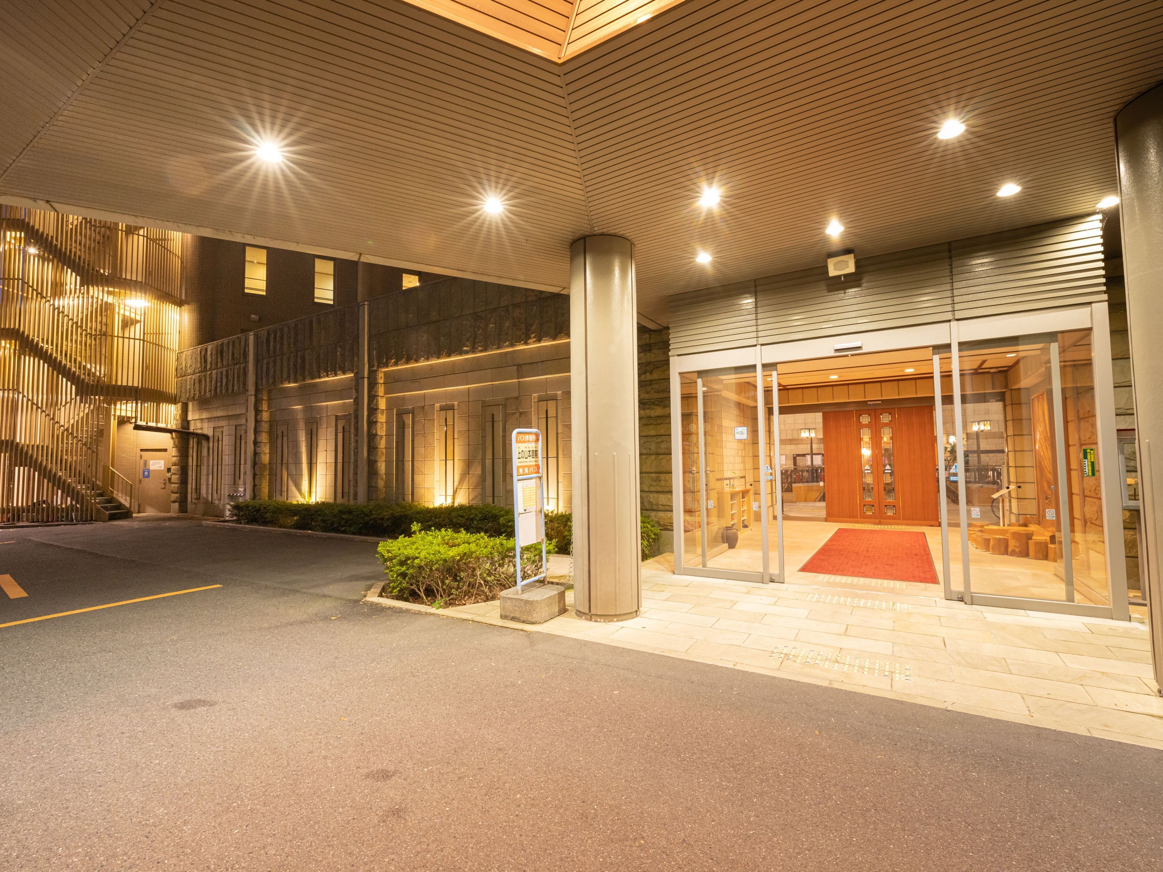 Entrada de hotel com tapete vermelho, escadas e porta de vidro.