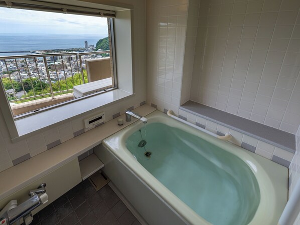 Un baño con una bañera grande, una ventana con vistas a la ciudad y un inodoro.