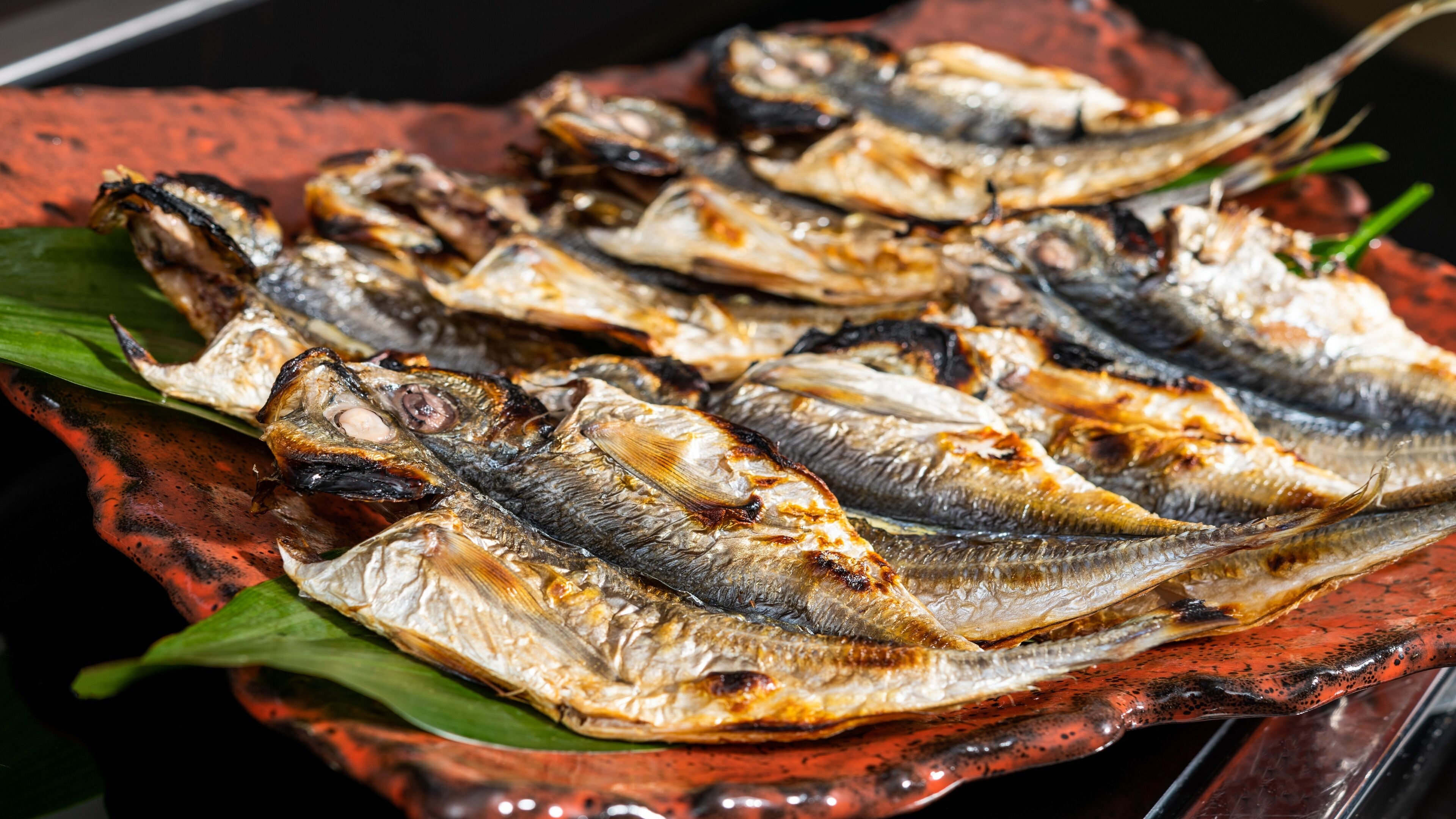Grilled fish arranged on a red platter with green leaves.