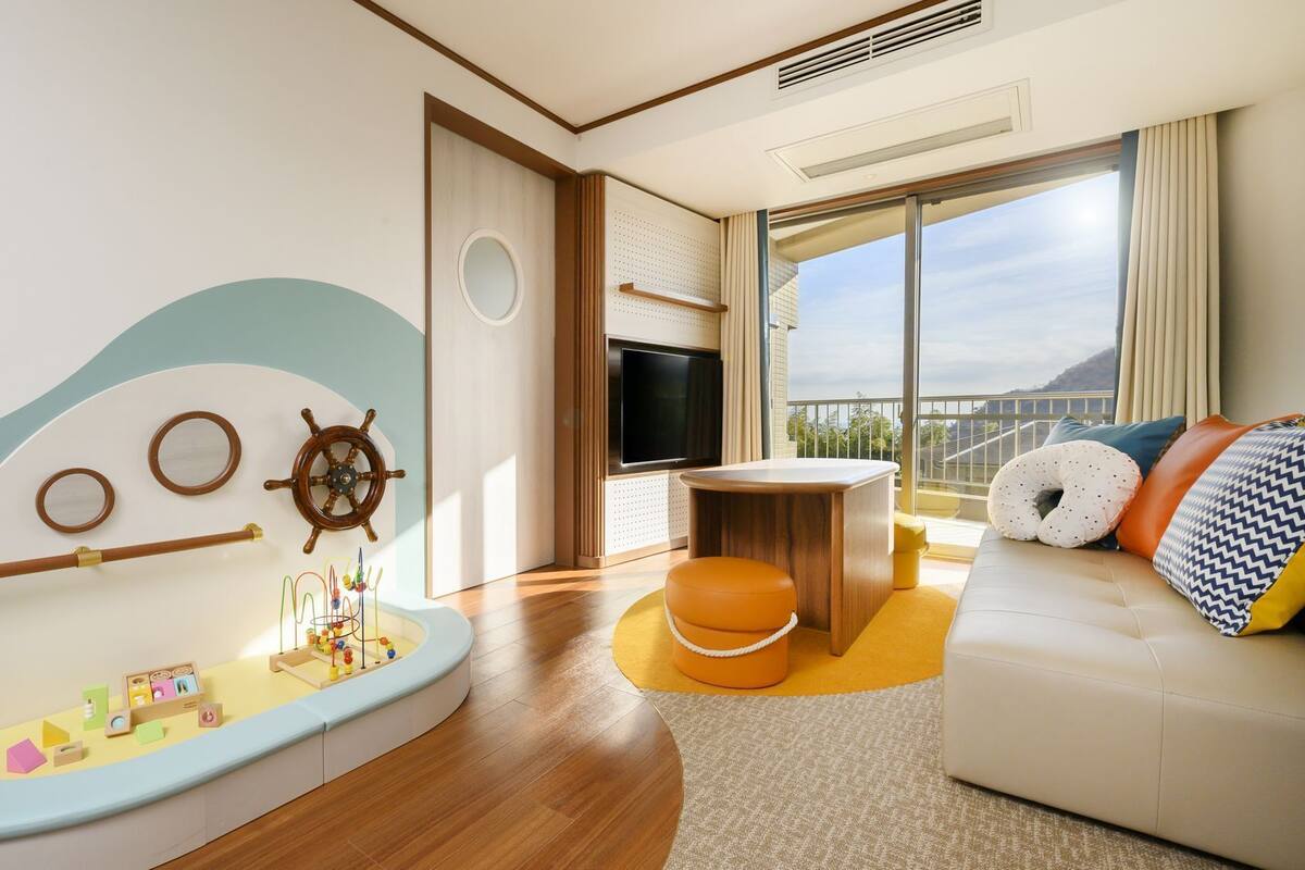 Een moderne woonkamer met een nautisch thema, inclusief een scheepsschroef, een hoekje voor kinderen, een bank met kussens en een groot raam met uitzicht.