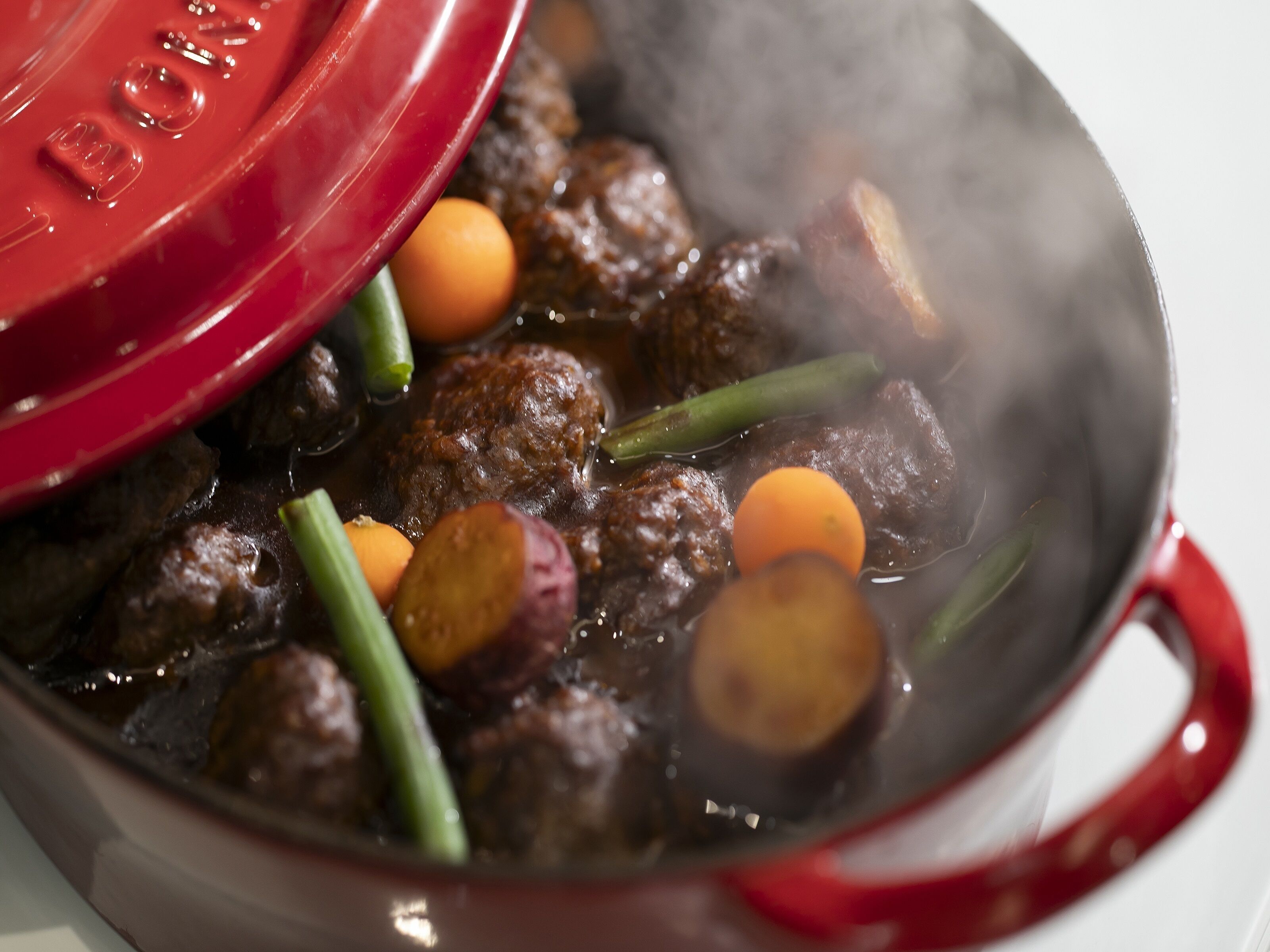 Una olla con tapa roja que contiene carne y verduras, probablemente en proceso de cocción.