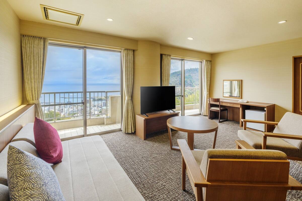 Hotelkamer met een groot balkon, een flatscreen televisie, een bureau en een bank.