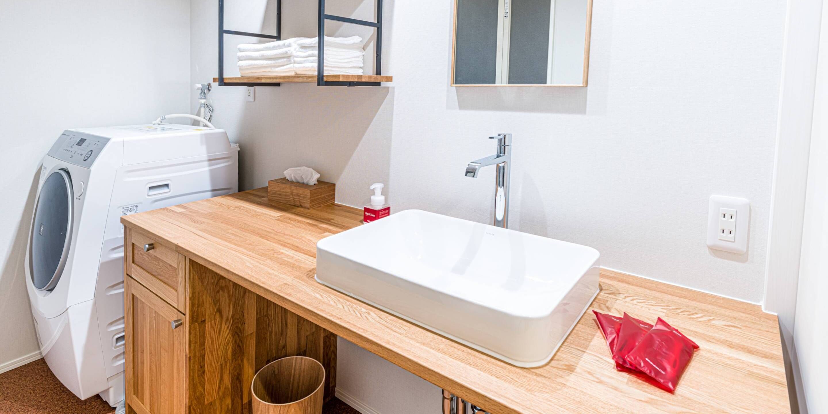 A modern bathroom with a wooden vanity, a built-in washing machine, a white sink, and a mirror above the mirror.