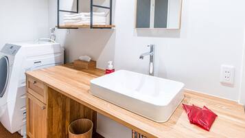 A modern bathroom with a wooden vanity, a built-in washing machine, a white sink, and a mirror above the mirror.