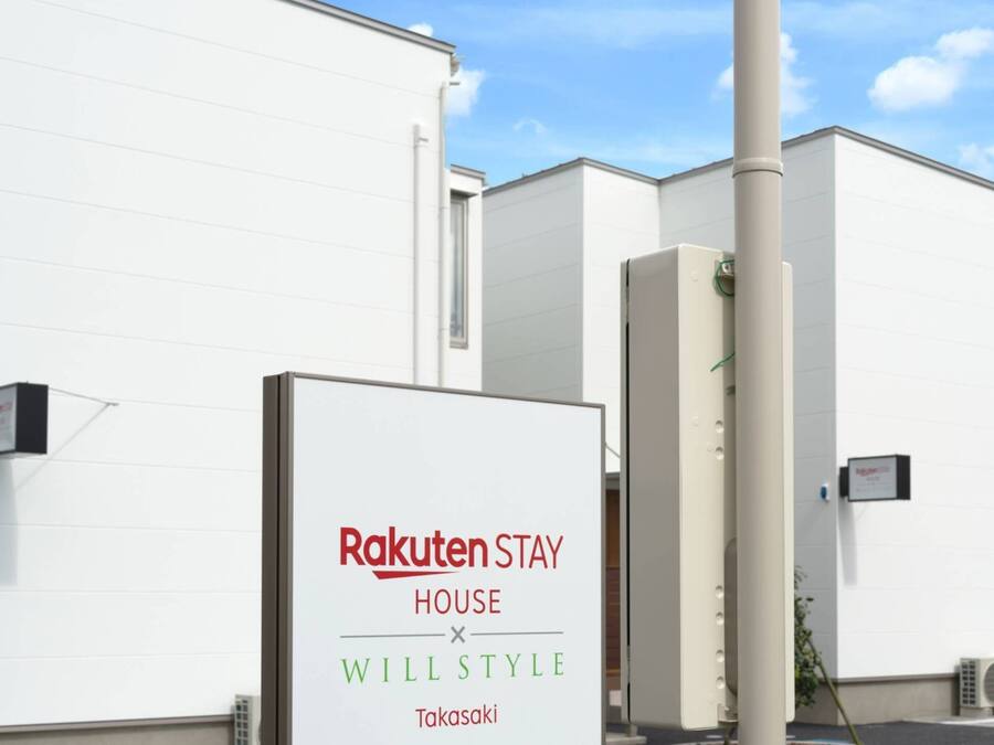 A sign for Rakuten Stay House x Will Style in a modern building with white walls and air conditioning units.