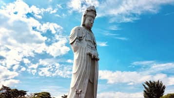 A large white statue of a figure with a long robe, standing against a blue sky with clouds.