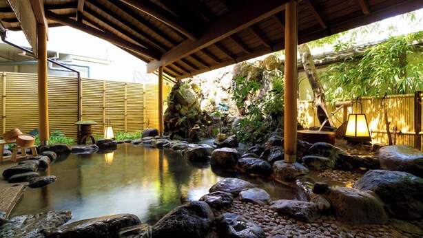 Ein traditionelles japanisches Onsen mit Holzdach, einem von Steinen gesäumten Thermalbad und Bambuswänden.