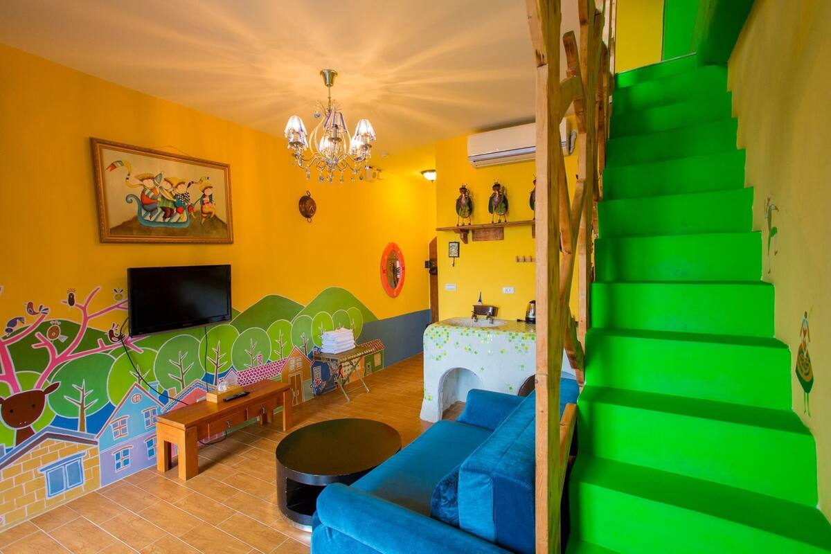 Una sala de estar con televisor, sofá y un mural colorido.