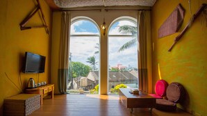 A room with a TV, wooden furniture, a bench, and a view of buildings and palm trees through large windows. - Castillo Kenting (Hengchun)
