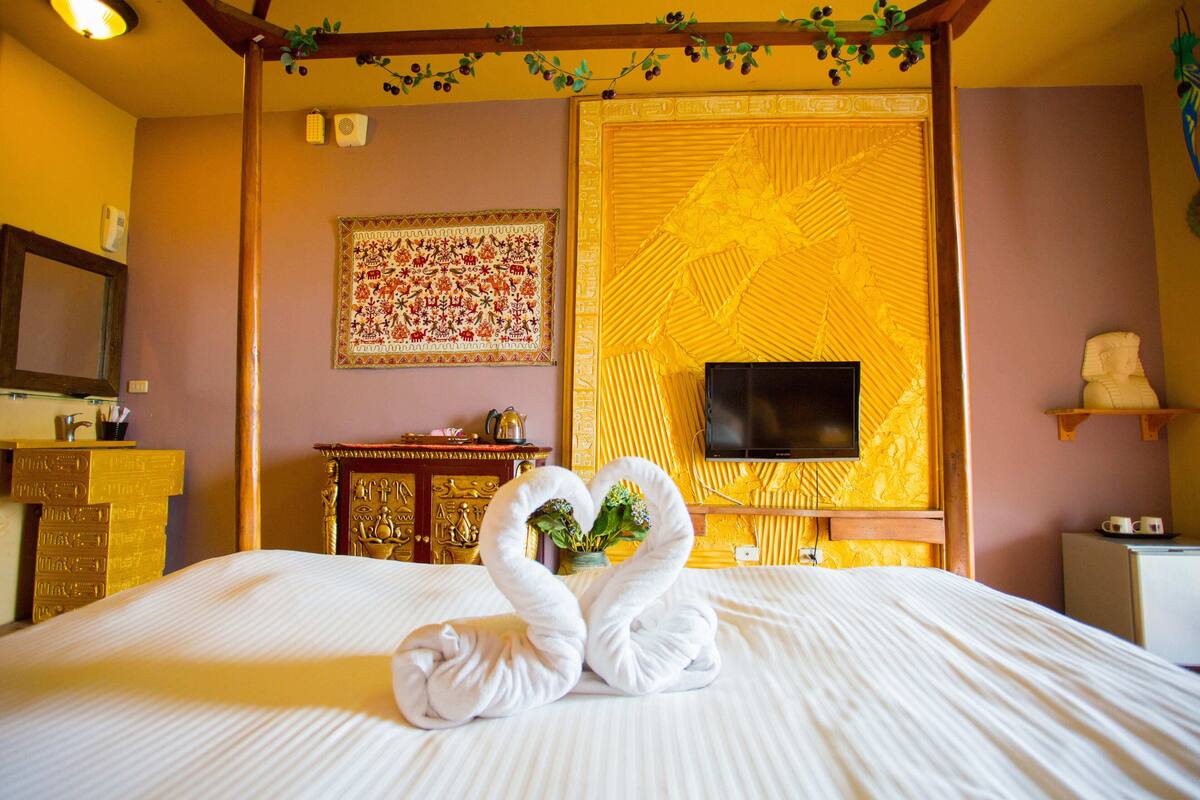 Habitación de hotel con cama, televisor, un adornado muro y una estatua.