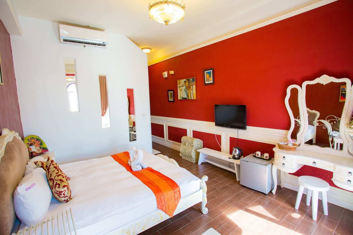 Una habitación de hotel con cama, tocador con espejo, televisor y un refrigerador pequeño.