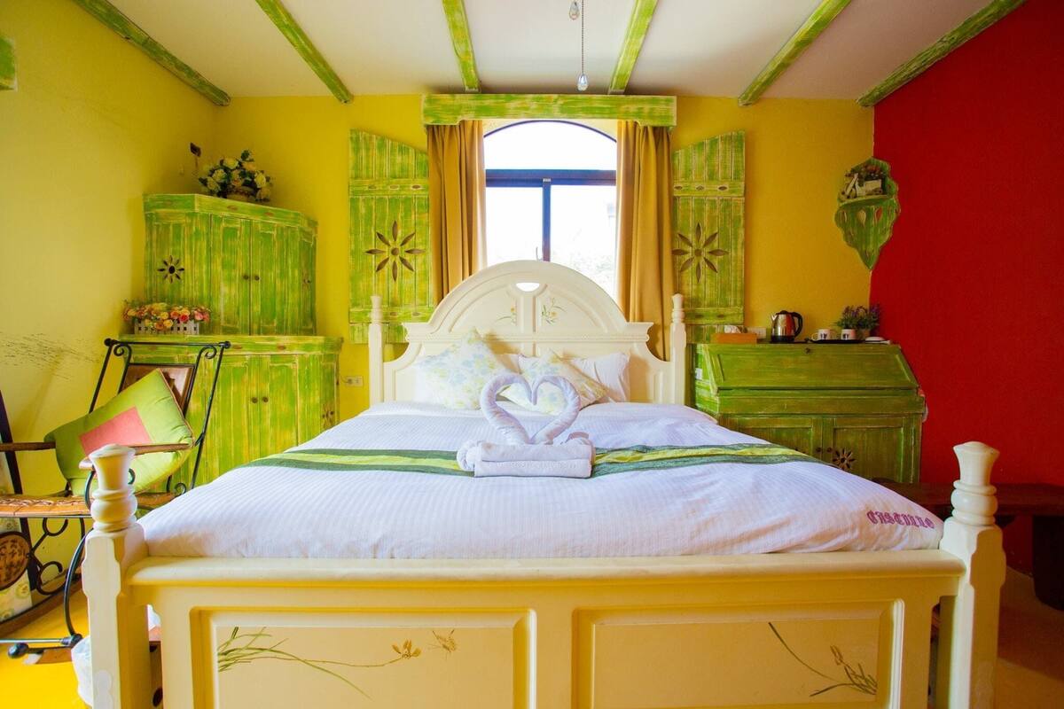 Una cama con cabecera blanca, un mueble verde y una pared roja.