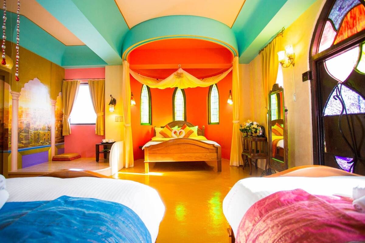 Una habitación luminosa y colorida con una cama grande, una cama más pequeña y una ventana con cortinas.