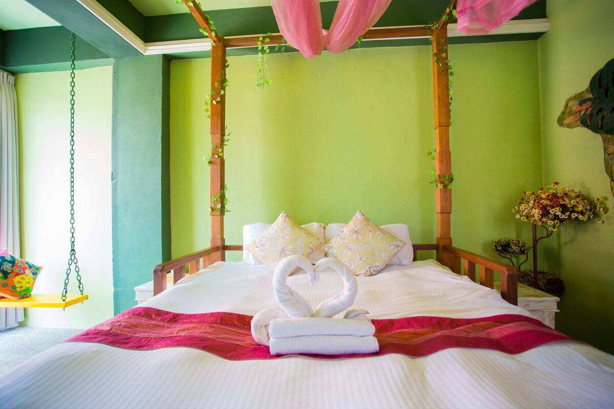 Una cama con una toalla dispuesta en forma de corazón, una hamaca colgante y una planta decorativa.