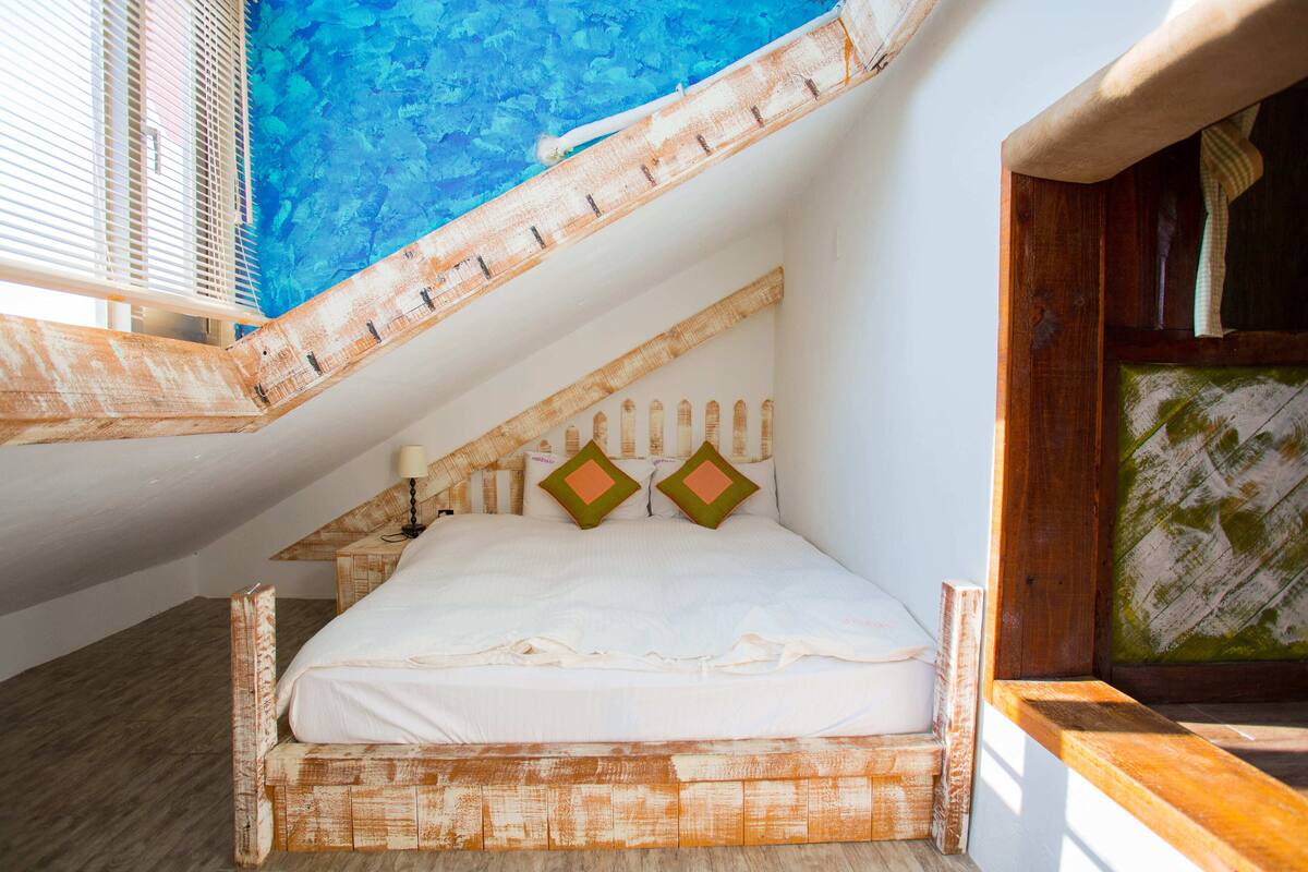 Un dormitorio con techo inclinado, estructura de cama de madera y vista del cielo a través de un tragaluz.