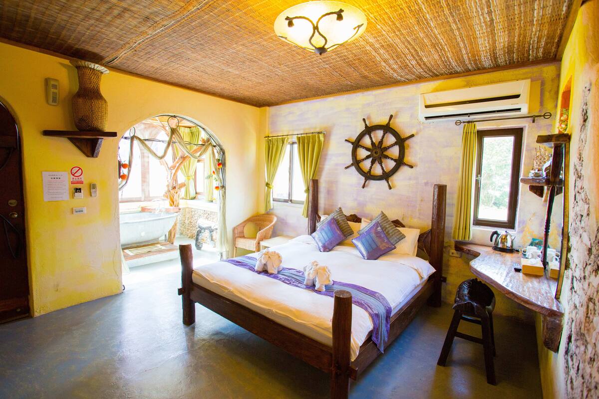 Una habitación con cama, escritorio y silla. Se observa un timón de barco en la pared y un equipo de aire acondicionado sobre el escritorio.