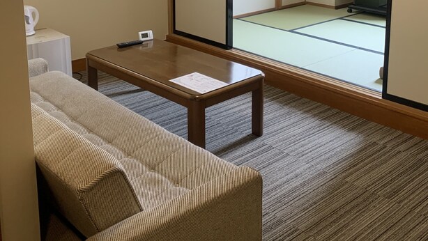 Ein traditioneller japanischer Raum mit Tatami-Böden, einem niedrigen Holztisch, einer Couch und Schiebetüren zu einem weiteren Tatami-Raum.