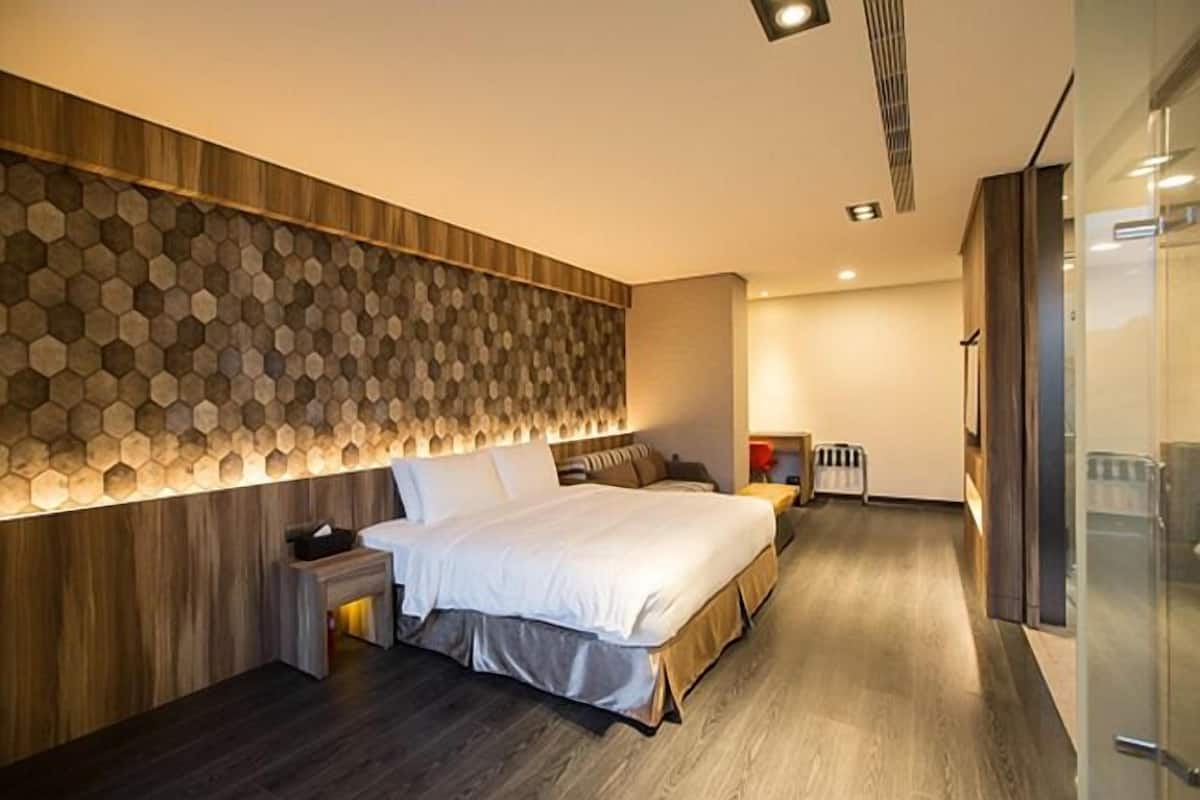 Habitación de hotel moderna con una cama grande, cabecero de madera, calefacción integrada y mampara de ducha de vidrio.